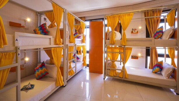 Quarto com beliches, cada um com cortinas amarelas, e um chão luminoso com azulejos.