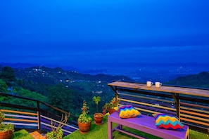 A bench with colorful cushions and a view of a cityscape at dusk. - Gostops Mussoorie (Dehradun)