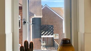 A window with a view of a brick building, a cactus plant, and a ceramic vase.