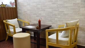 Un petit coin repas comprenant deux chaises en bois, une table et un pouf rond.