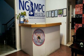 A reception desk with a sign for NGBMPC Hostel, a logo for Galerian Business Men, and several framed documents on the wall. - Ngbmpc Hostel (Puerto Galera)