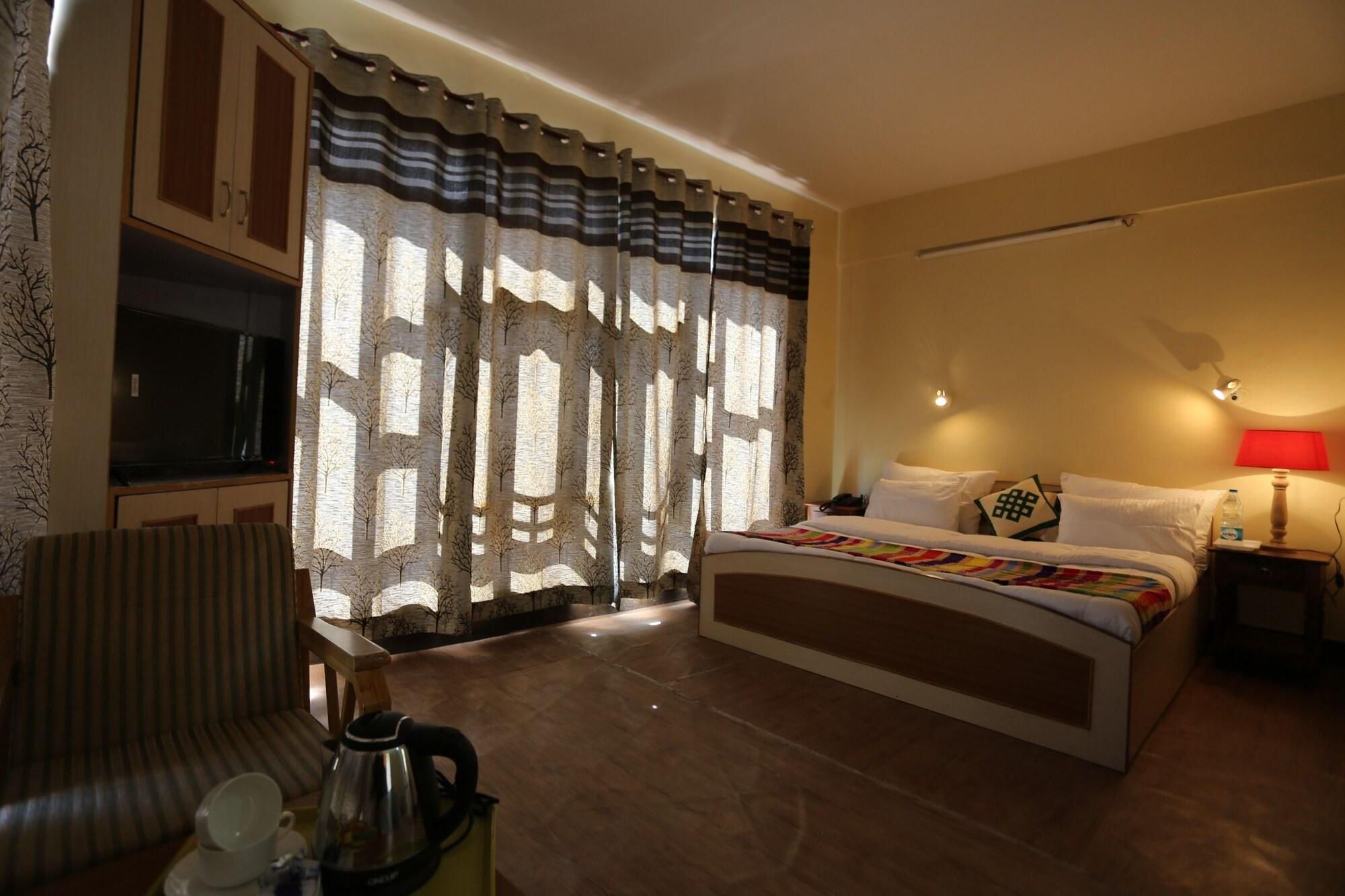 A hotel room with a bed, a desk, a chair, a television, and a window with curtains.