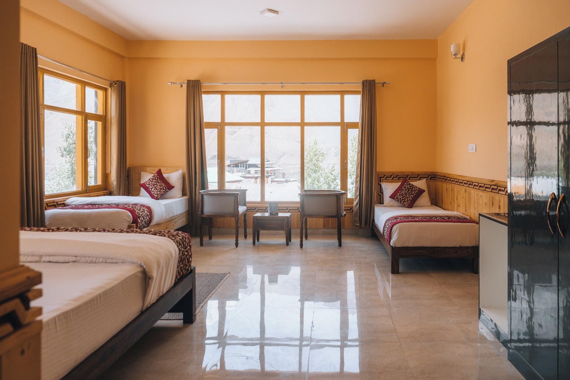 A hotel room with two beds, a small table, chairs, and a large window with a view.