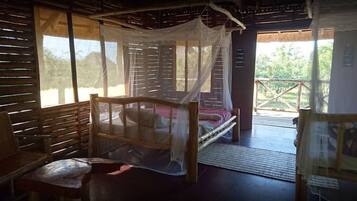 A room with a bed under a mosquito net, a bench, and a view of the outdoors.