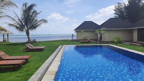 A swimming pool with a view of the ocean, surrounded by palm trees and lounge chairs. - The Kelong Trikora Resort - Bintan Island (Bintan Island)