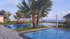 A swimming pool with a wooden deck, palm trees, and a view of the sea. - The Kelong Trikora Resort - Bintan Island (Bintan Island)