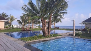 A swimming pool with a wooden deck, palm trees, and a view of the sea. - The Kelong Trikora Resort - Bintan Island (Bintan Island)