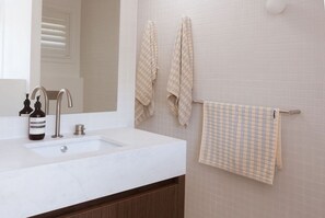 Ein Badezimmer mit einem weißen Waschbecken, zwei Wasserhähnen, einem Spiegel und einem Handtuchhalter mit zwei Handtüchern.