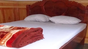 Uma cama de madeira com colchão e almofadas brancas, um cobertor vermelho e piso de azulejos.