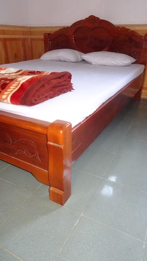 Ein hölzernes Bett mit weißer Matratze und Kissen, eine rote Decke und ein Fliesenboden.