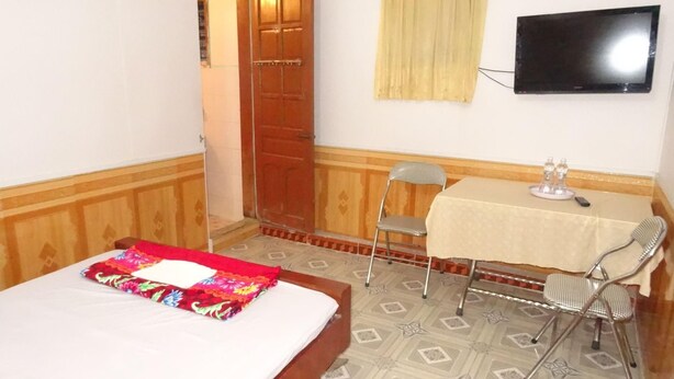 Quarto com uma cama, mesa, duas cadeiras, televisão e uma porta.