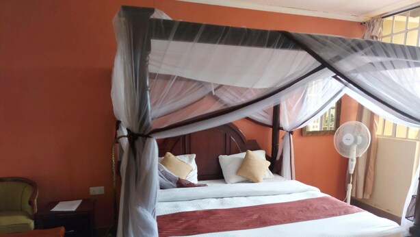 Ein Bett mit Baldachin, ein Nachttisch, ein Sessel und ein Standventilator.