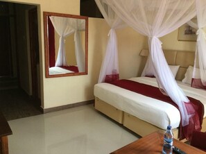 A hotel room with a bed, a bedside table with a bottle, a lamp, and a mirror with a canopy. - Treat House Resort (Kisii)