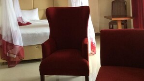 Ein Hotelzimmer mit einem Bett, einem roten Sessel, einem Nachttisch aus Holz und einem roten Vorhang.