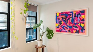 Een kamer met een raam, een plant in pot en een kleurrijk abstract schilderij aan de muur.