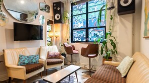 A living room with a sofa, two armchairs, a coffee table, a TV, and a window with a view of a building. - Hosier Lane Hideaway Events & City Life (Melbourne)