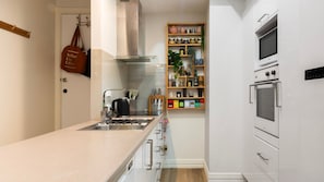 A modern kitchen with a built-in oven, a coffee machine, and a wooden shelf with kitchen utensils. - Hosier Lane Hideaway Events & City Life (Melbourne)