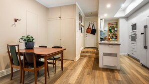 Een kleine keuken met moderne apparaten, een eethoek met een houten tafel en stoelen, en een klein portaal met kapstok.