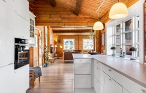 Eine geräumige Küche mit einer zentralen Kochinsel, Holzbalken an der Decke und einem Essbereich mit einer Couch und Tisch.
