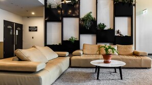Eine moderne Lobby mit zwei beigefarbenen Sofas, einem runden Couchtisch mit Topfpflanze und schwarzen, vertikalen Pflanzgefäßen mit Grünpflanzen.