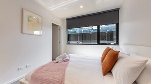 Ein modernes Schlafzimmer mit Bett, Kissen, einem Fenster und einer Tür.