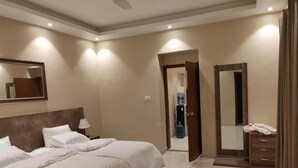 A hotel room with a large bed, a bedside table, a mirror, and a wardrobe. - Hamsun (Karachi)