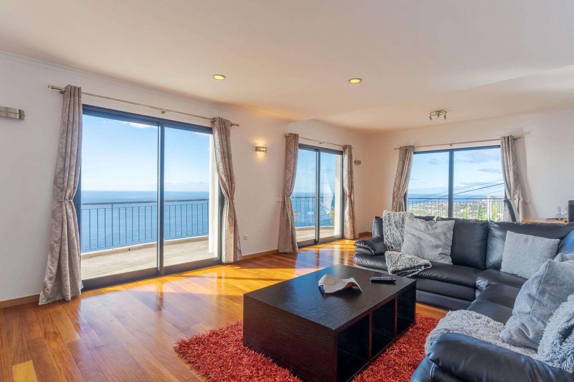 Ein geräumiges Wohnzimmer mit einer großen Couch, einem Couchtisch und Meerblick durch raumhohe Fenster.