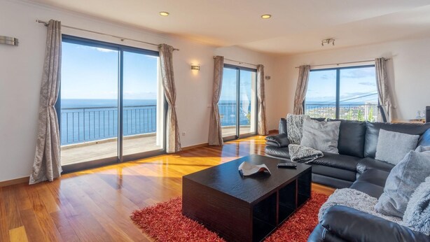 Ein geräumiges Wohnzimmer mit einer großen Couch, einem Couchtisch und Meerblick durch raumhohe Fenster.