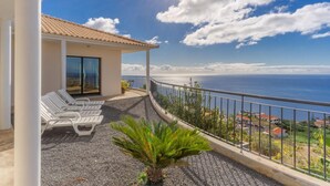 Ein Balkon mit weißen Liegestühlen, einer kleinen Palme und Blick aufs Meer.