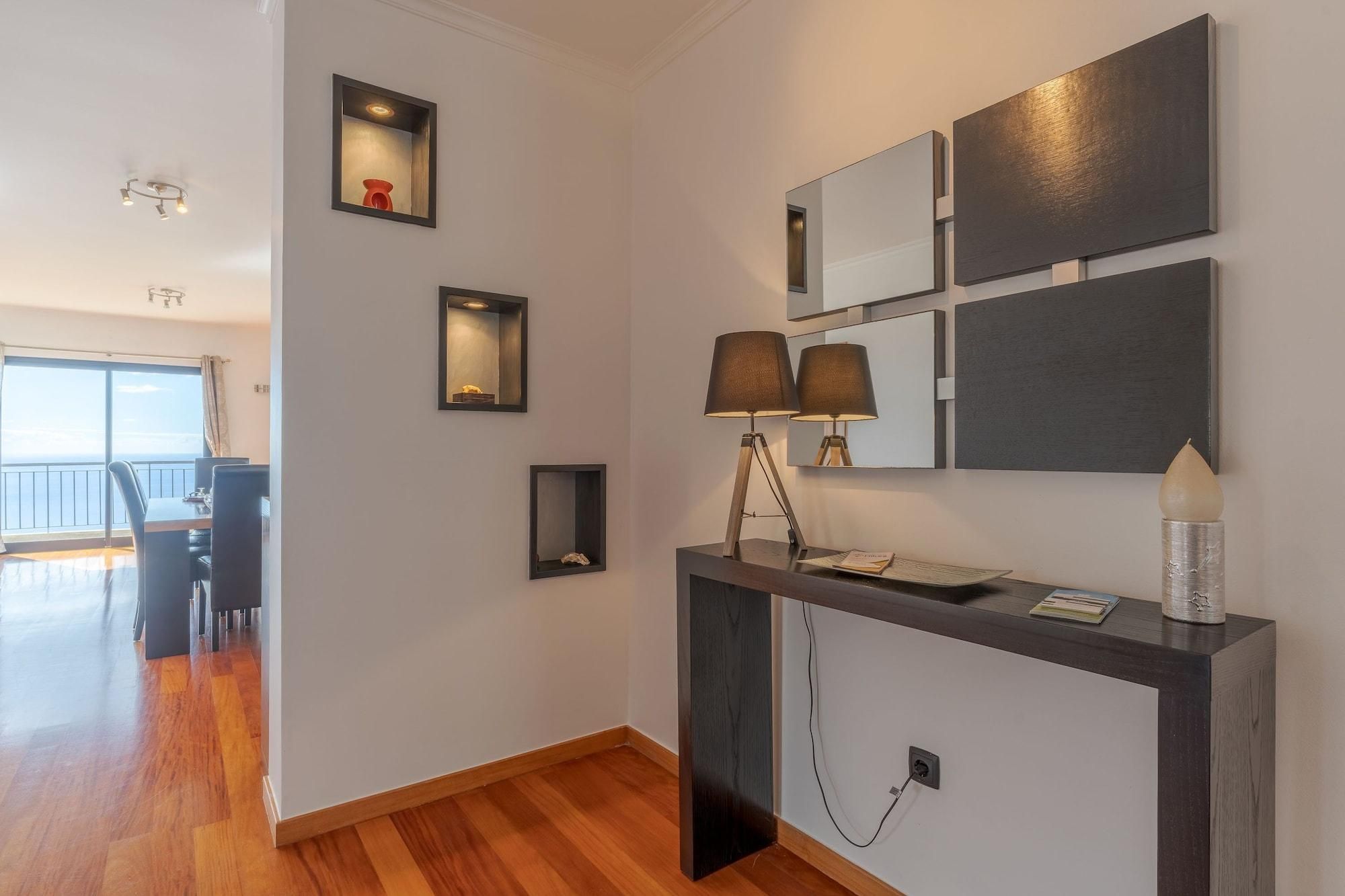 Ein modernes Hotelzimmer mit Holzboden, einem Schreibtisch mit Lampe und einem großen Fenster mit Meerblick.