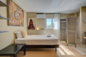 Ein Schlafzimmer mit Bett, Schreibtisch, Fenster, Klimaanlage und einer Schiebetür zum Badezimmer.