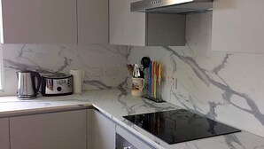A kitchen with a black stovetop, white cabinets, a stainless steel range hood, and a marble backsplash. - Percy Place (Bath)