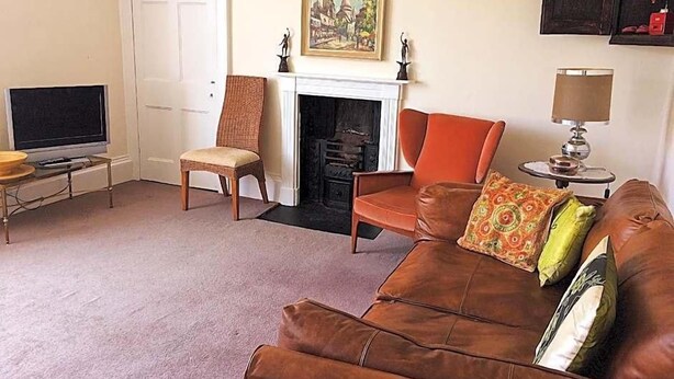 A living room with a brown leather sofa, a wooden chair, a television, a fireplace, and a painting on the wall. - Percy Place (Bath)
