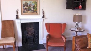 A living room with a fireplace, a red armchair, a brown sofa, and a small table with a lamp. - Percy Place (Bath)