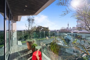 A modern balcony with glass railings, potted plants, and a view of a city skyline. - The Margot by Homello (Auckland)