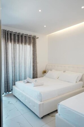 A modern bedroom with a large bed, a bedside table, and a curtain. - Vila Mucodemi (Ksamil)