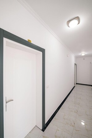 A hallway with white walls, a marble floor, and doors with a number sign. - Vila Mucodemi (Ksamil)