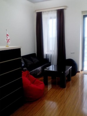 Un salon avec un canapé noir, un fauteuil poire rouge, une table basse et un petit drapeau posé sur une étagère.