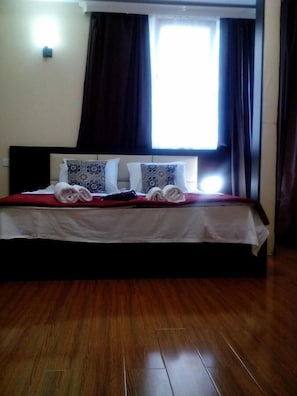 Une chambre d’hôtel avec un lit, des oreillers, une couverture rouge et un plancher en bois.