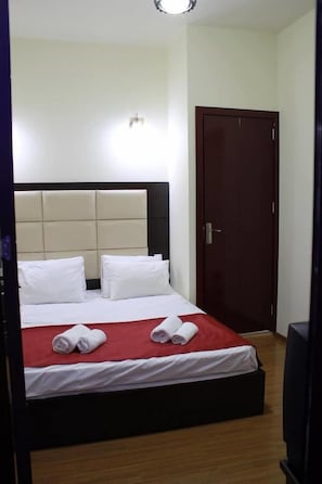Une chambre d’hôtel avec un lit, un plancher en bois, une tête de lit blanche et une porte fermée.