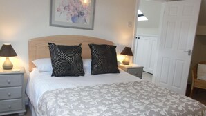 A bedroom with a bed, two nightstands, two lamps, a door, and a framed picture on the wall. - High Grange Cottages (Bedale)