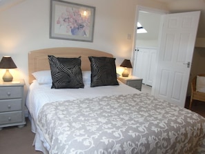 Quarto com cama, duas mesas de cabeceira, duas luminárias, uma porta e um quadro na parede.