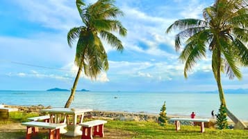 Un cadre idyllique au bord de la plage, avec des palmiers, des tables de pique-nique et une vue sur l’océan.