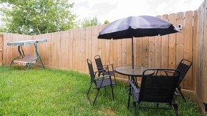 A backyard with a wooden fence, a round glass table, four black chairs, and a blue umbrella. - Modern 3BR | 3 Baths | Near NRG & Med Center (Houston)