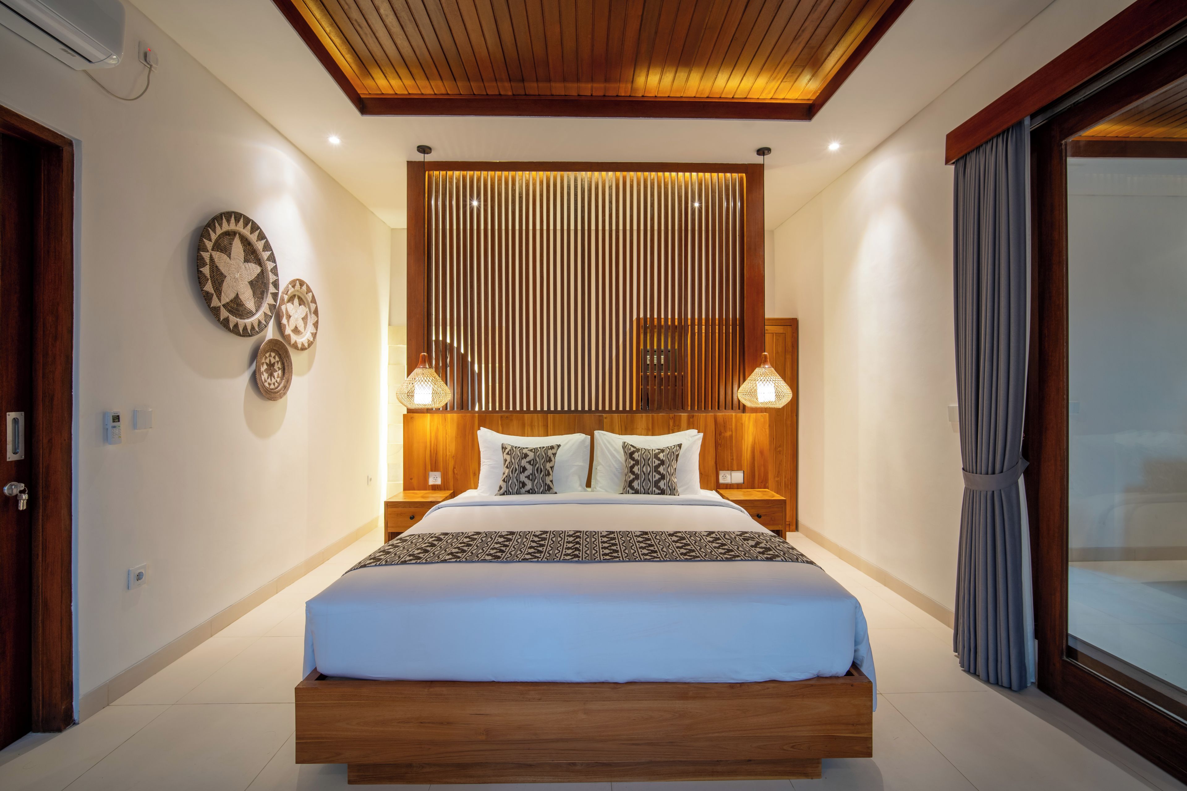 Un dormitorio moderno con cabecera de madera, cama grande, lámparas de noche y decoración mural.