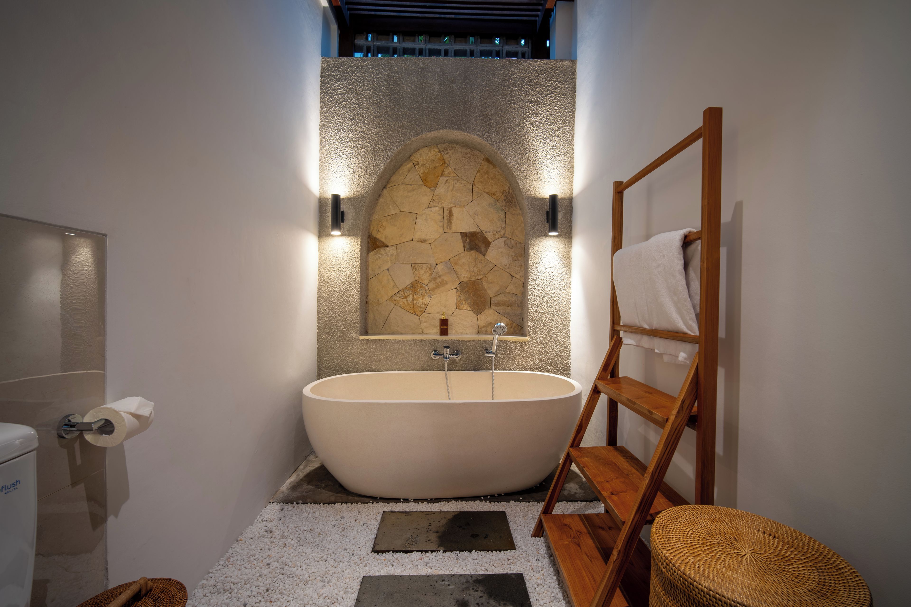 Un baño moderno con una bañera independiente, pared de piedra y muebles de madera.