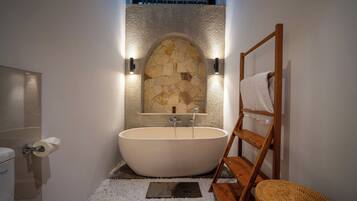 Un baño moderno con una bañera independiente, pared de piedra y muebles de madera.