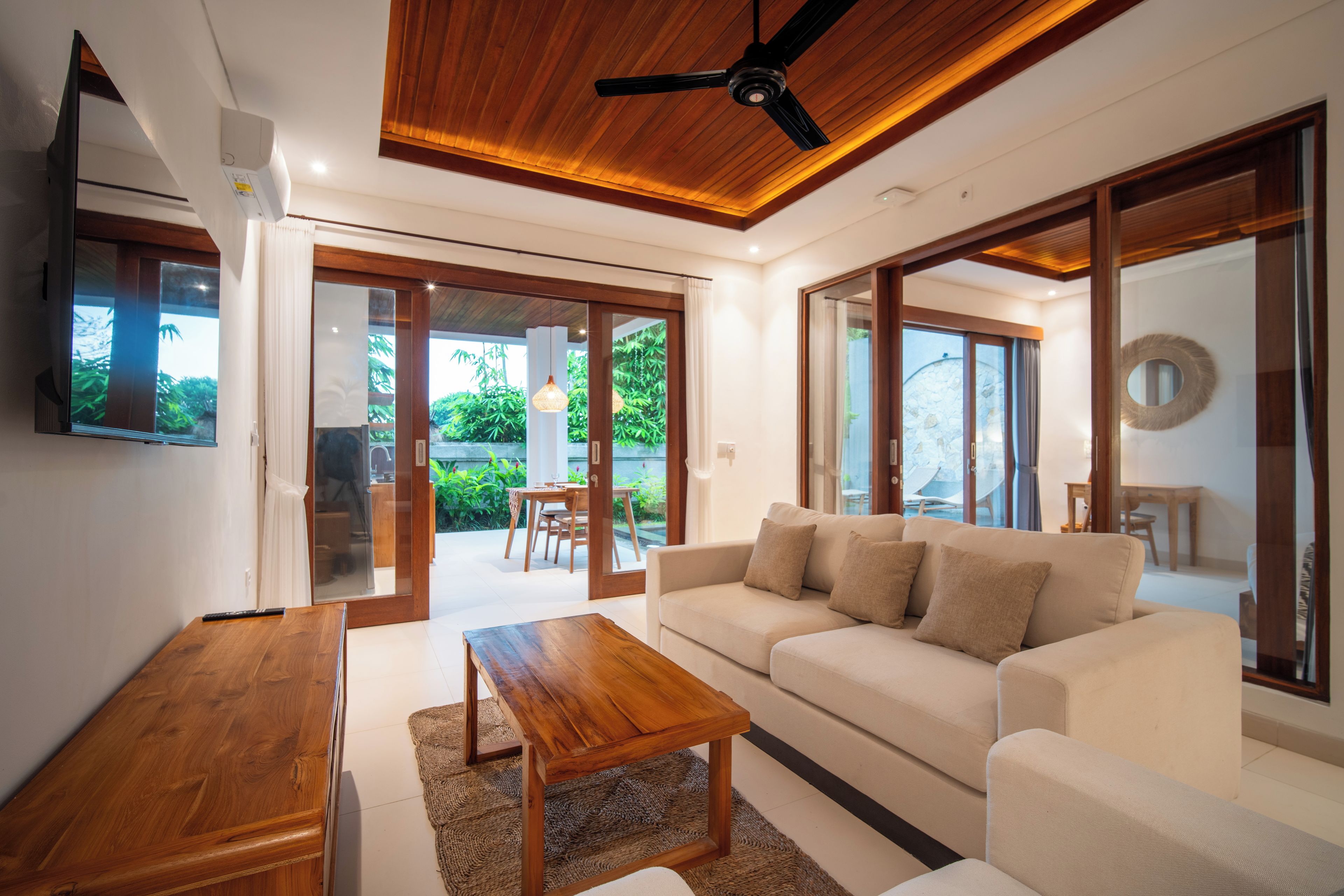 Una sala moderna con techo de madera, un sofá blanco, una mesa de centro de madera y un televisor.