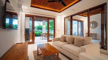 Una sala moderna con techo de madera, un sofá blanco, una mesa de centro de madera y un televisor.