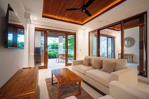 Una sala moderna con techo de madera, un sofá blanco, una mesa de centro de madera y un televisor.